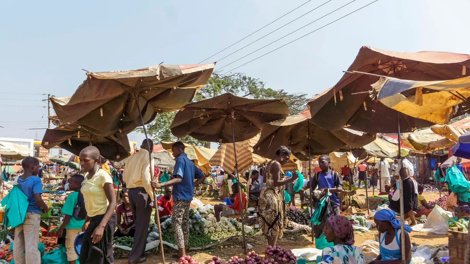 Vendors and shoppers at a busy open-air market shaded by umbrellas